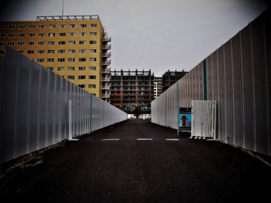 Uzak binalara doğru giden uzun metal çitler arasındaki dar yol.