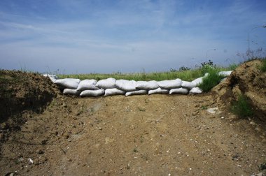 Kum torbaları mavi gökyüzünün altında toprak yol boyunca bariyer oluşturuyorlar