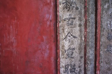 Kırmızıya boyanmış duvarın yanında Çinli karakterlerin yer aldığı yıpranmış taş sütun.