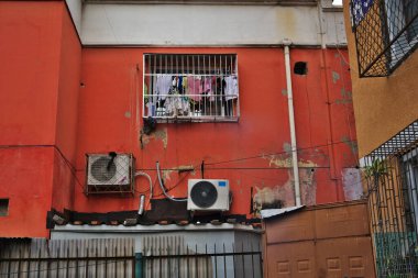 Yıkanmış kırmızı duvar. Çitli pencere klimaları çamaşır borularını asıyor.