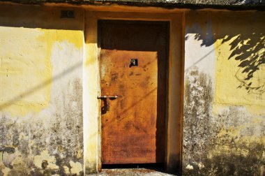 Eski sarı lekeli duvardaki paslı metal kapı.