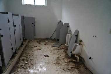 Kirli zemini ve bozuk tezgahları olan terk edilmiş bir tuvalet.