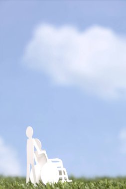 Tekerlekli sandalyedeki kişi yeşil çimlerin üzerinde kağıttan yapılmış. 