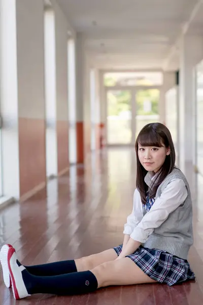 portrait of Asian teenage girl in school uniform sitting on the floor in hallway