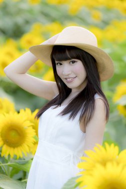 Ayçiçeği tarlasında beyaz elbise ve hasır şapka giyen güzel Asyalı kadın. 