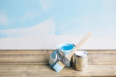 Beyaz ahşap arka planda mavi boya kovaları ve boya fırçası, yenileme araçları