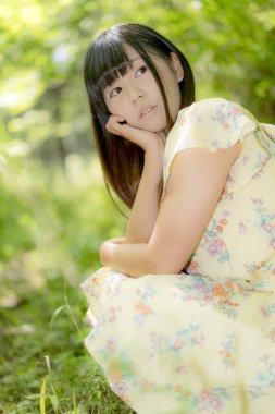 Elbise giyip yaz parkında poz veren Asyalı genç bir kadın. Tasasız kız dışarıda dinleniyor. 