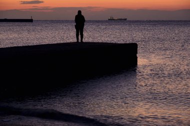 Gün batımında denizde bir balıkçının silueti..
