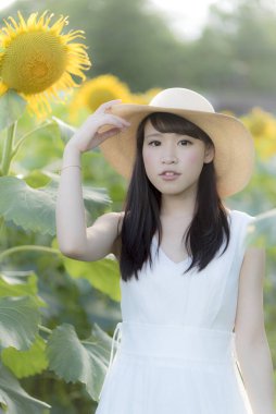 Ayçiçeği tarlasında beyaz elbise ve hasır şapka giyen güzel Asyalı kadın. 