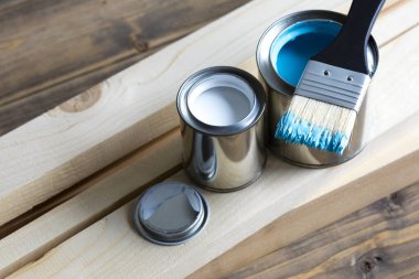 Ahşap yüzeyde boya kutuları ve fırçalar var.