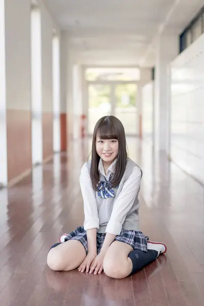 portrait of Asian teenage girl in school uniform sitting on the floor in hallway