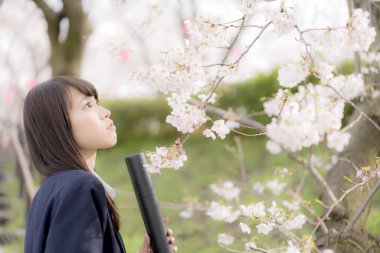 Okul üniformalı güzel bir Asyalı kız, bahar parkında poz veriyor.