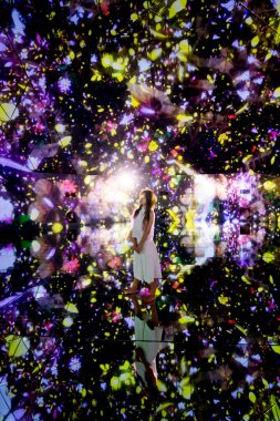 Güzel Asyalı kadın, karanlık oda stüdyosunda renkli ışıklar ve konfetiyle poz veriyor.