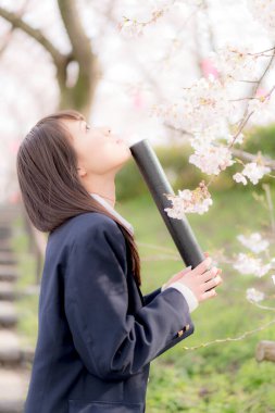 Okul üniformalı güzel bir Asyalı kız, bahar parkında poz veriyor.