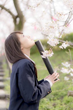 Okul üniformalı güzel bir Asyalı kız, bahar parkında poz veriyor.