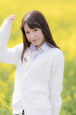 Okul üniforması giyen güzel Asyalı kız sarı çiçek tarlasında poz veriyor. 