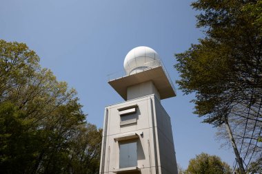 Yeşil ağaçların arasında duran uzun beton radar kulesi