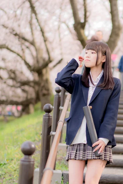 beautiful Asian girl in school uniform with blueprint tube holder posing in spring park