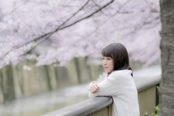 Beautiful asian teenager girl posing in park with cherry blossoms