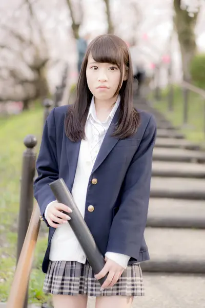 beautiful Asian girl in school uniform with blueprint tube holder posing in spring park