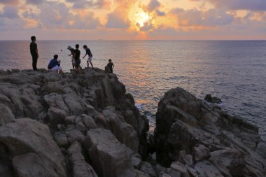 Kayalık sahilde durup deniz manzarasının güzelliğine bakan insanlar. 