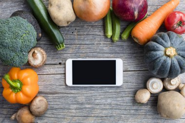 Ahşap arka planda taze taze organik sebzeli akıllı telefonun üst görüntüsü