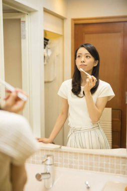 Genç ve güzel bir kadın evde aynada dişlerini fırçalıyor. 