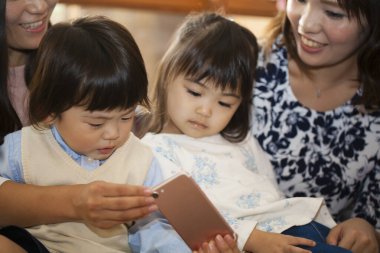 Çocuklar gülümseyen kadınlarla akıllı telefon izliyorlar.