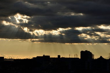 Şehir binalarının üzerinde gün batımında karanlık bulutlar.