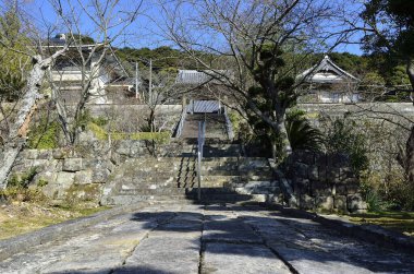 Çıplak ağaçların arasındaki geleneksel Japon binalarına doğru atılan taş adımlar.