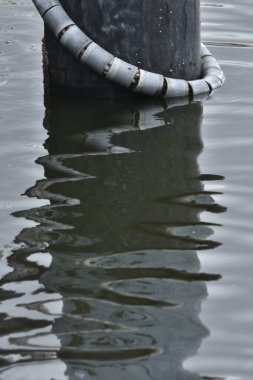 Su yüzeyine yansıyan yıpranmış direğin etrafını saran gri boru.
