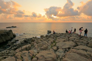 Turistler kayaların üzerinde durur ve güzel günbatımının tadını çıkarırlar. 