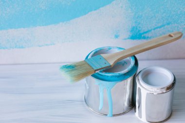 Beyaz ahşap arka planda mavi boya kovası ve boya fırçası, yenileme araçları