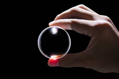 Siyah zemin üzerinde şeffaf cam top tutan el.