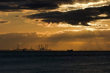 Deniz ve şehrin üzerinde güzel bir günbatımı. Güneş bulutların arasında parlıyor..