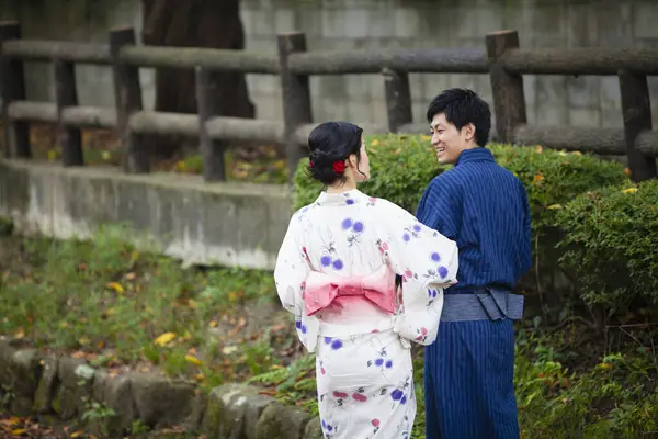 young Japanese couple wearing traditional kimono in summer park, back view