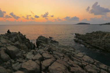 Kayaların üzerinde duran ve güzel günbatımının tadını çıkaran bir adam 