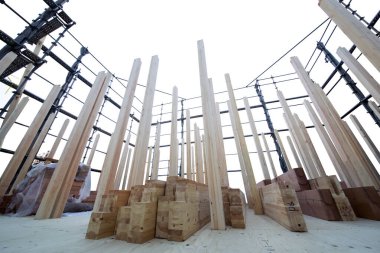 Parlak gökyüzünün altındaki inşaat alanında dikey duran tahta kirişler.