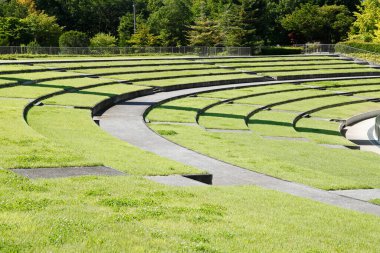 Yeşil çimenler ve ağaçlarla çevrili eğimli amfi tiyatro koltukları.