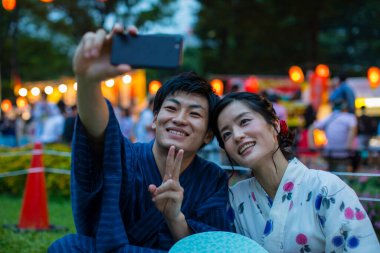 Geleneksel kimono giyen genç Japon çift akşam parkında akıllı telefondan selfie çekiyor.