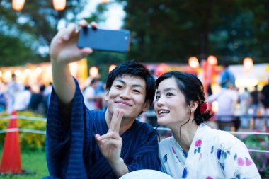 Geleneksel kimono giyen genç Japon çift akşam parkında akıllı telefondan selfie çekiyor.