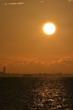 Deniz ve şehrin üzerinde güzel bir günbatımı. Güneş bulutların arasında parlıyor..