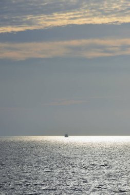 Gün batımında denizde bir gemi, bulutlu bir gökyüzü