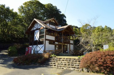 Geleneksel ahşap ev açık mavi gökyüzünün altında ağaçlarla çevrili.