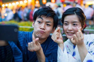 Geleneksel kimono giyen genç Japon çift akşam parkında akıllı telefondan selfie çekiyor.