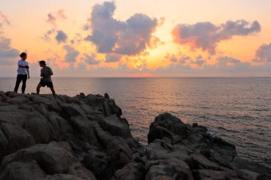 Kayaların üzerinde duran ve güzel günbatımının tadını çıkaran adamlar. 
