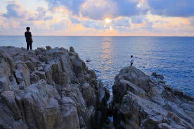 Kayaların üzerinde duran ve güzel günbatımının tadını çıkaran adamlar. 