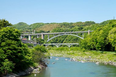 Nehir boyunca uzanan kemerli köprü yemyeşil ağaçlarla çevrili.