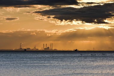 Deniz ve şehrin üzerinde güzel bir günbatımı. Güneş bulutların arasında parlıyor..