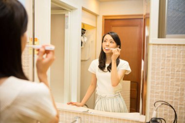 Genç ve güzel bir kadın evde aynada dişlerini fırçalıyor. 